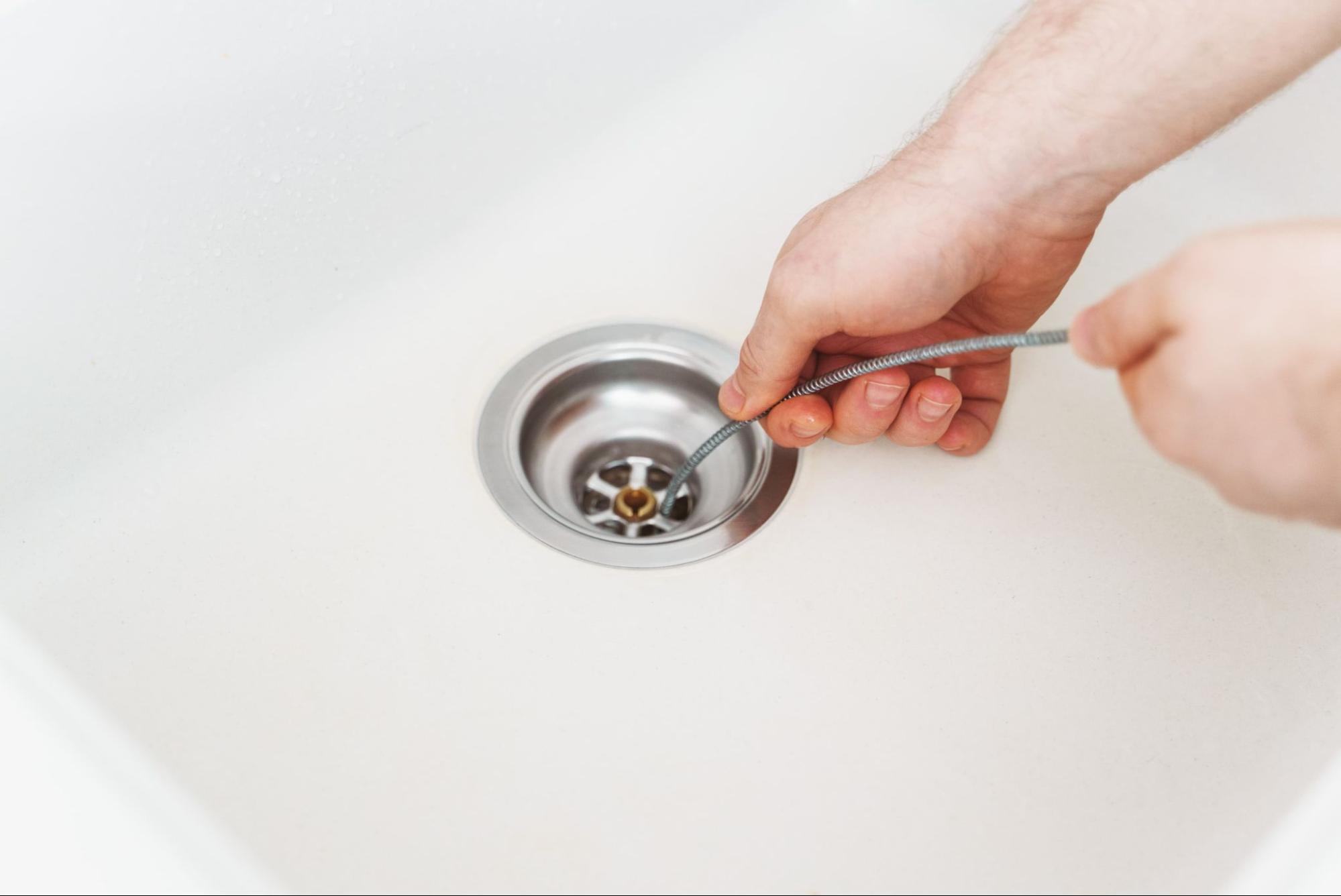 plumber using a drain snake on clogged kitchen sink